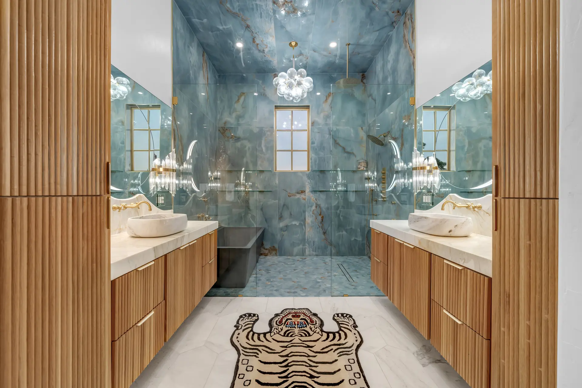 A bathroom with teal stone walls and wood-front floating vanities