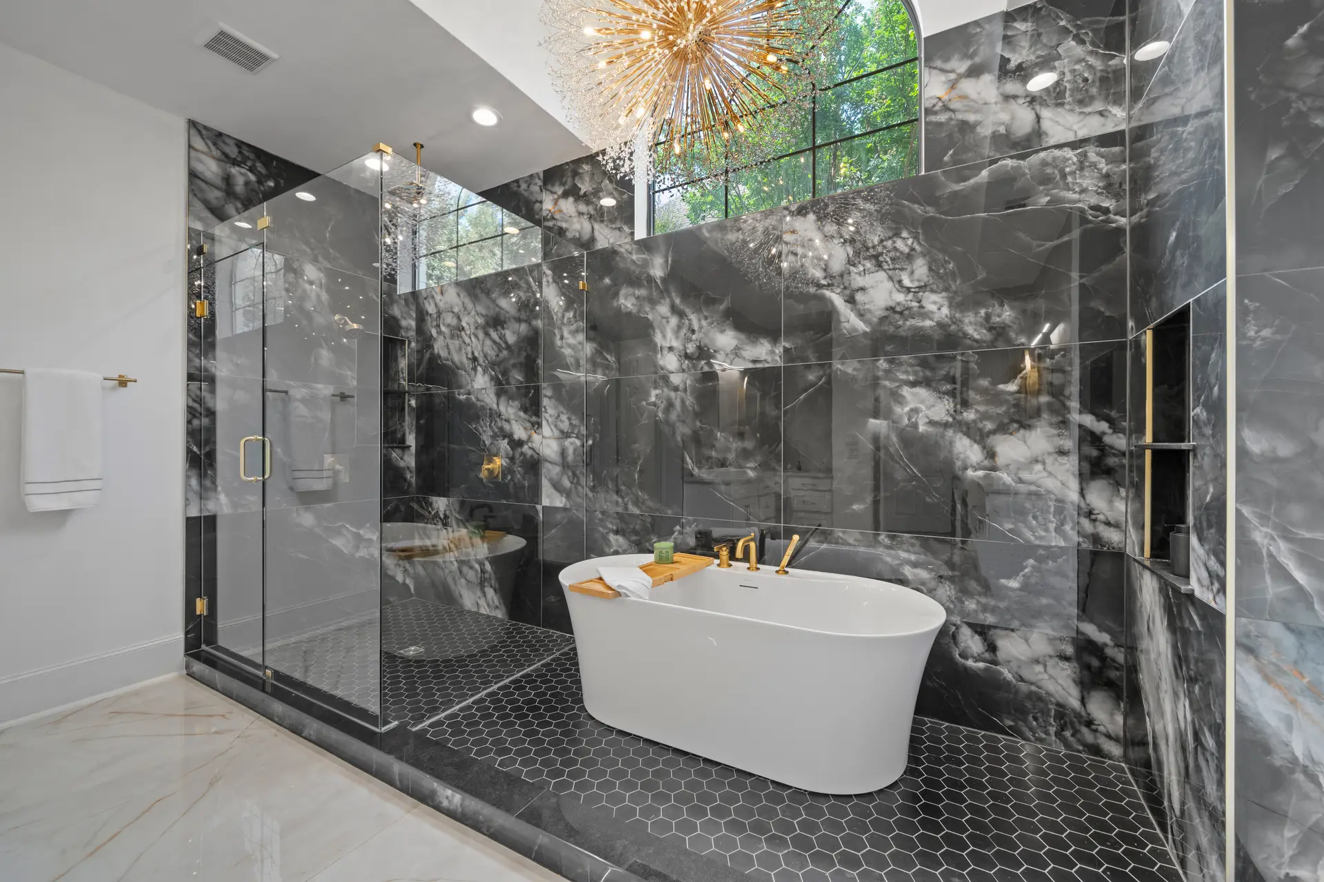 A bathroom with black marble walls, a glass shower and a freestanding tub