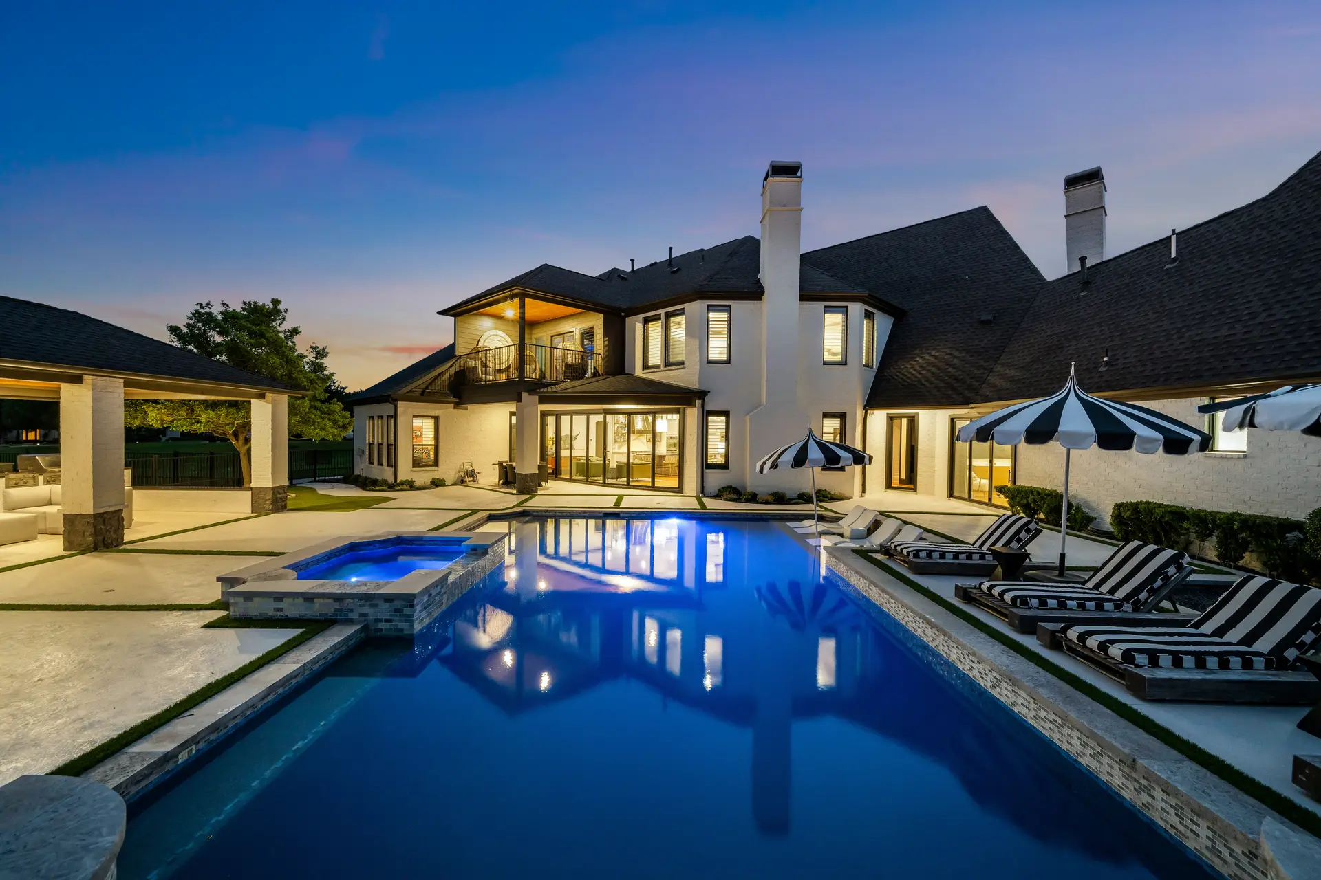 A stucco home with a lit backyard pool and patio at night
